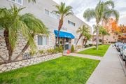 Bellflower multi-family for rent - A building with a blue awning and a sign that says "The Cave" is surrounded by palm trees.
