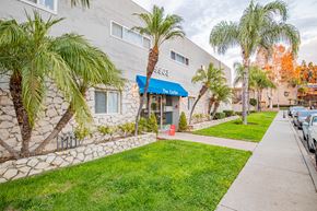 Bellflower multi-family for rent - A building with a blue awning and a sign that says "The Cave" is surrounded by palm trees.