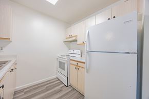 Santa Clarita multi-family for rent - A white refrigerator stands in a kitchen with wooden cabinets and a stove.