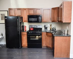 Trenton apartment for rent - A black refrigerator stands next to a black stove in a kitchen with wooden cabinets.
