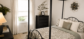 Essex townhouse for rent - A bedroom with a four poster bed, a nightstand with a lamp, and a window with curtains.