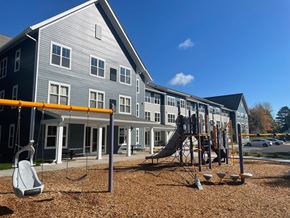 Duluth apartment for rent - A playground with a swing set and a slide in front of a grey building.