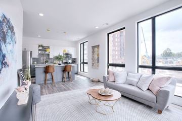 Omaha apartment for rent - A modern living room with a grey sofa and a kitchen area in the background.