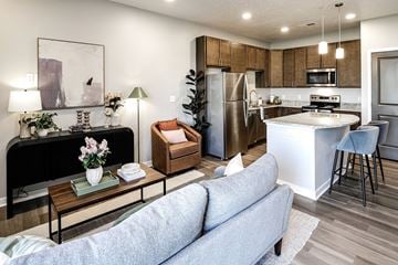 Columbus apartment for rent - A modern living room with a grey sofa, a coffee table with a vase of flowers, a black piano, and a kitchen area in the background.