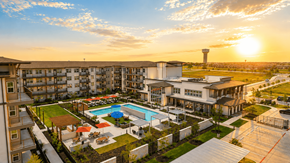 Pflugerville apartment for rent - A sunset view of a large apartment complex with a pool and a tower in the distance.