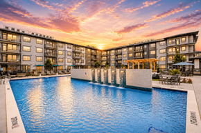 Mckinney apartment for rent - A large swimming pool in front of a building with a sunset in the background.