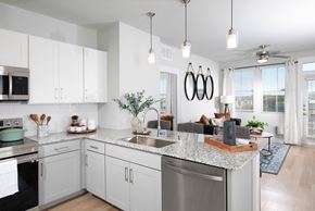 Las Vegas apartment for rent - a kitchen with stainless steel appliances and granite countertops opening up to a living room at a senior apartment community