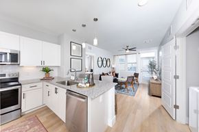 Glendale apartment for rent - a kitchen with stainless steel appliances and granite countertops opening up to a living room at a senior apartment community