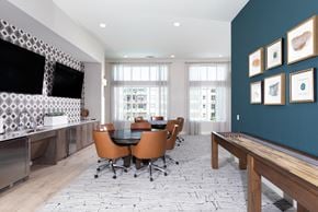 Glendale apartment for rent - a game room with card tables and chairs, a television, and a table shuffleboard at a senior apartment community