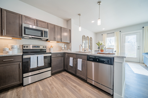Charlotte apartment for rent - a kitchen with stainless steel appliances and granite countertops opening up to a living room at a senior apartment community
