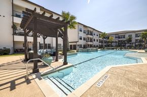Houston apartment for rent - a resort-style pool with a lounge area under a wooden pergola at a senior apartment community