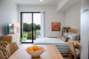 Naples apartment for rent - A bowl of oranges sits on a wooden table in a well-lit room with a bed and a television.at The Teale Golden Gate in Naples, FL, 34116