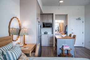 Naples apartment for rent - A bedroom with a bed, a desk with a chair, and a kitchen area with a refrigerator, microwave, and cabinets.at The Teale Golden Gate in Naples, FL, 34116