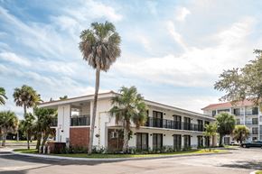 Naples apartment for rent - A white building with a balcony and a palm tree in front.at The Teale Golden Gate in Naples, FL, 34116