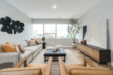 Troy apartment for rent - A modern living room with a grey sofa, a black coffee table, and a large abstract painting on the wall.