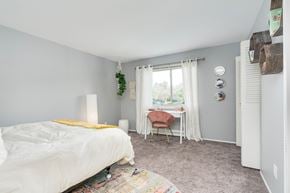 Okemos apartment for rent - A bedroom with a white bed and a chair by the window.