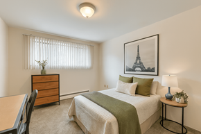 East Lansing apartment for rent - A bedroom with a bed, nightstand, and a painting of the Eiffel Tower on the wall.