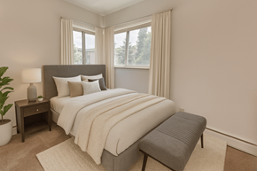 East Lansing apartment for rent - A bedroom with a large bed, a nightstand, a lamp, a potted plant, and a window with curtains.
