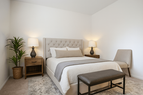 Okemos apartment for rent - A bedroom with a large bed, a bench, and a potted plant.