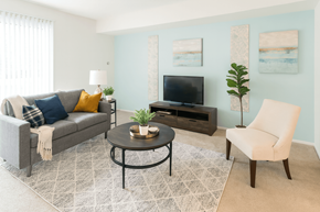 East Lansing apartment for rent - A living room with a grey couch, a black coffee table, a white chair, and a television.