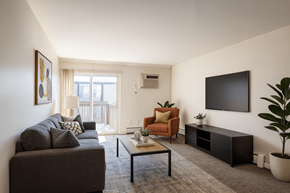 East Lansing apartment for rent - A living room with a grey couch, a brown armchair, a black coffee table, and a flat screen TV mounted on the wall.