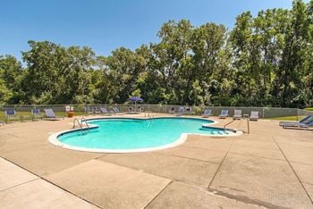 A small pool surrounded by trees and chairs.