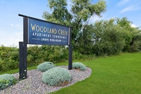 Saginaw townhouse for rent - A sign for Woodland Creek Apartment Townhomes stands in front of a grassy area.