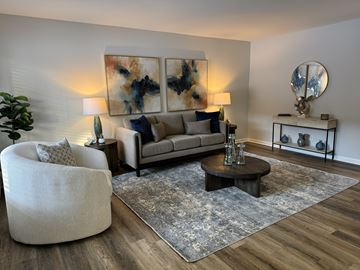 Royal Oak apartment for rent - A modern living room with a grey sofa, a round chair, a coffee table, and a large abstract painting on the wall.