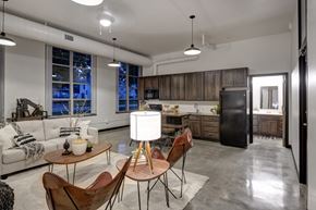 West Des Moines apartment for rent - A modern kitchen and living room with a white sofa, wooden chairs, and a black refrigerator.