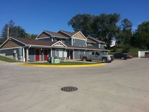 Cedar Rapids apartment for rent - A building with a grey roof and a red door is surrounded by a parking lot.