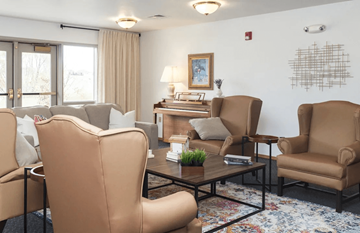 Adel apartment for rent - A living room with a brown chair in the foreground and a white wall with a picture frame and a fire alarm.