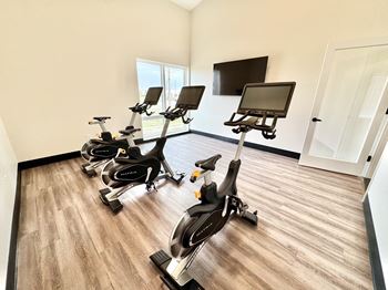 A room with a row of stationary bikes and a tv mounted on the wall.