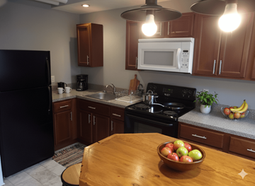Buffalo apartment for rent - A kitchen with a black refrigerator, wooden cabinets, a black stove, and a wooden table with a bowl of fruit on it.