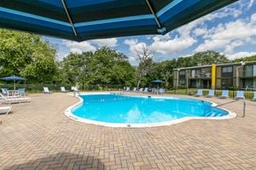 Woodridge apartment for rent - A swimming pool surrounded by a brick patio and lounge chairs under a blue canopy.