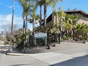 Fullerton apartment for rent - A sign for "Idylwood" stands in front of a building with a brick wall and palm trees.