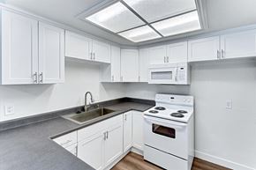 Fullerton apartment for rent - A white kitchen with a stove, sink, and cabinets.