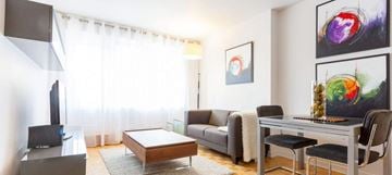 Montreal apartment for rent - A living room with a grey couch, a black chair, a wooden coffee table, a television, and a painting on the wall.