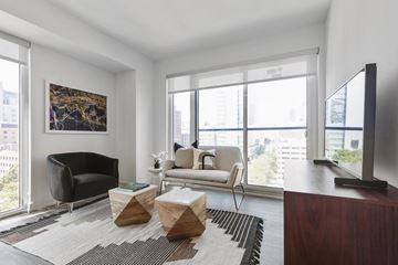 Toronto apartment for rent - A living room with a black chair, a white chair, a wooden coffee table, and a painting on the wall.