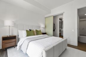 Toronto apartment for rent - A white bed with a white mattress and a white bed sheet with a white pillow and a white lamp on a wooden nightstand.