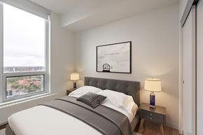 Calgary apartment for rent - A bedroom with a large bed and a window overlooking a cityscape.