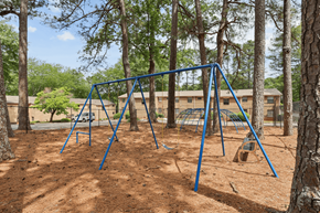 Decatur apartment for rent - A playground swing set in a wooded area with a building in the background.