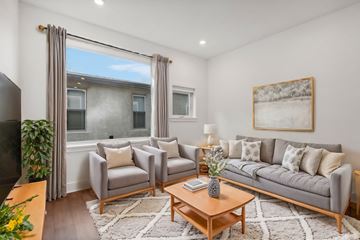 Philadelphia apartment for rent - A living room with a grey sofa, a grey armchair, a wooden coffee table, a white rug, a painting on the wall, and a window with curtains.
