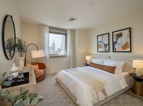 Philadelphia apartment for rent - A bedroom with a large bed, a round mirror, and a view of the city.