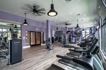 A gym with cardio machines and a ceiling fan