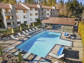 Mountlake Terrace apartment for rent - A swimming pool surrounded by sun loungers and umbrellas in front of apartment buildings.
