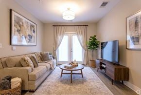 Sellersburg apartment for rent - A living room with a beige couch, a wooden coffee table, and a flat-screen TV mounted on the wall.