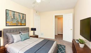 Louisville apartment for rent - A bedroom with a bed, a painting, a lamp, a rug, a plant, and a television.