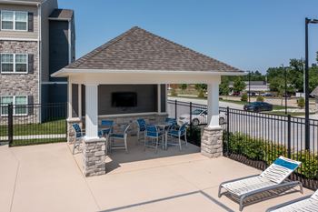 A gazebo with a stone pillar and a bench is in the foreground of a residential area.