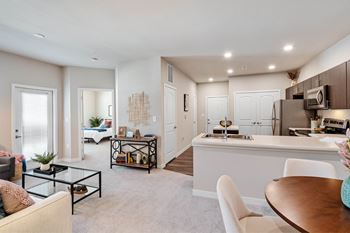 A modern living room with a white sofa, a glass coffee table, and a dining area with a white table and chairs.