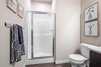 A bathroom with a toilet, a shower with a glass door, and towels hanging on a rack.